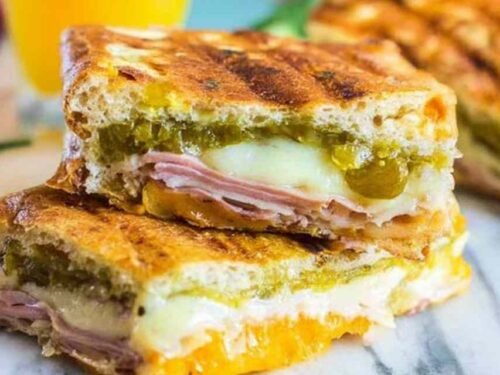 Ingredients for Cuban Sandwiches including ham, pork, pickles, and Swiss cheese on a cutting board.