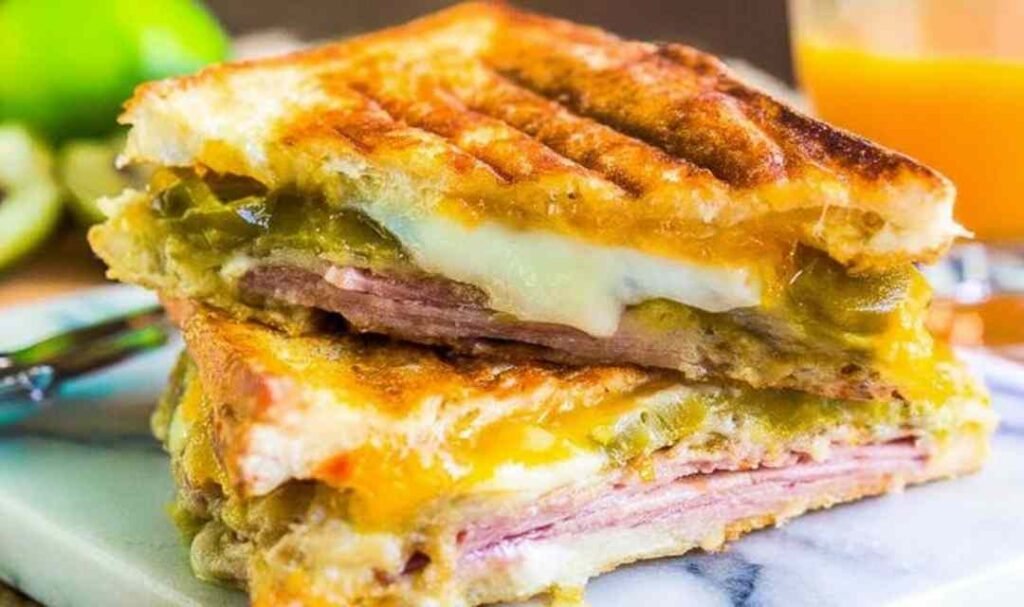 Ingredients for Cuban Sandwiches including ham, pork, pickles, and Swiss cheese on a cutting board.