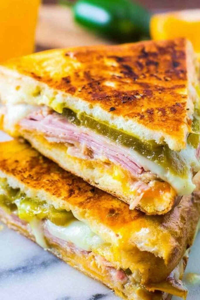 Ingredients for Cuban Sandwiches including ham, pork, pickles, and Swiss cheese on a cutting board.