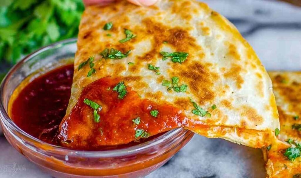 Crispy enchilada chicken quesadillas cut into wedges on a white plate served with red enchilada dipping sauce and fresh sliced avocado