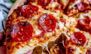 Homemade pizza recipe with crispy crust, melted mozzarella, and pepperoni sliced on a wooden board