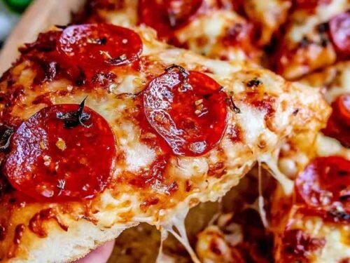 Homemade pizza recipe with crispy crust, melted mozzarella, and pepperoni sliced on a wooden board