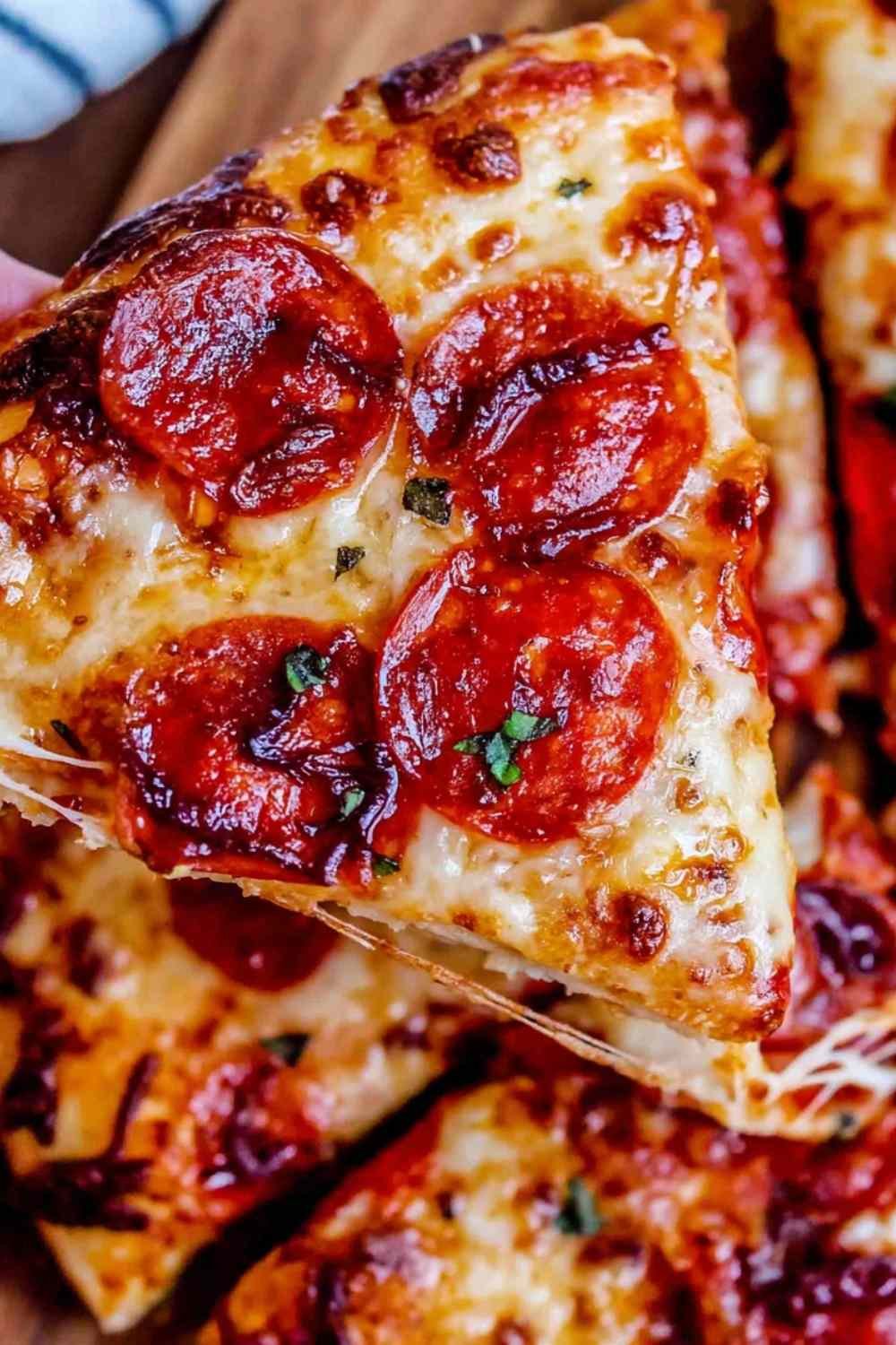 Homemade pizza recipe with crispy crust, melted mozzarella, and pepperoni sliced on a wooden board