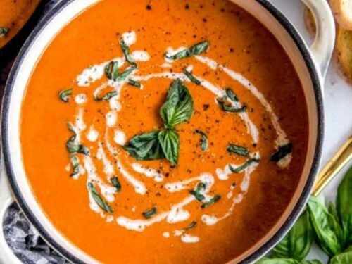 A bowl of creamy homemade tomato soup topped with fresh basil and a swirl of heavy cream
