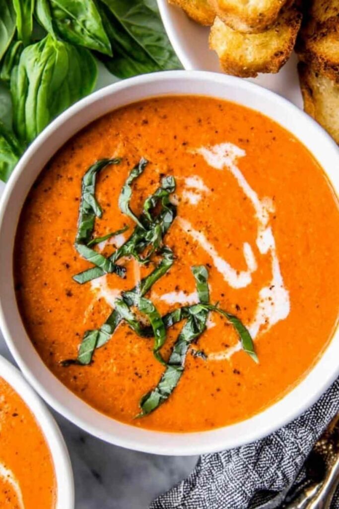 A bowl of creamy homemade tomato soup topped with fresh basil and a swirl of heavy cream