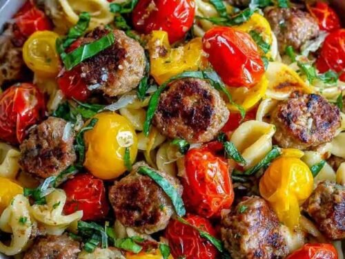 A shallow bowl of Italian sausage pasta with cherry tomatoes, green onions, and fresh basil garnish