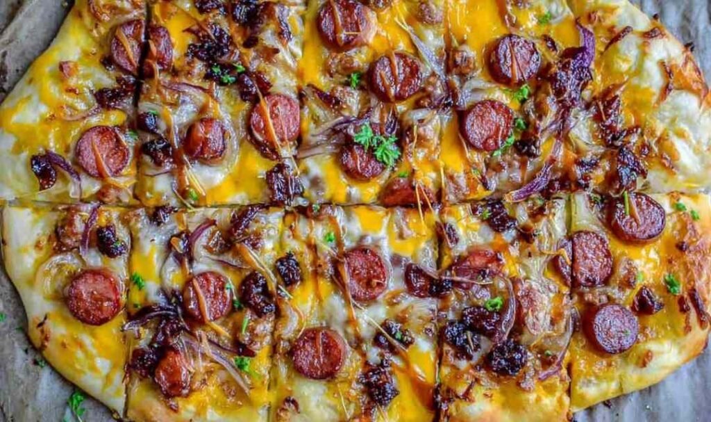 Sliced leftover hot dog pizza with caramelized onions and melted mozzarella on a wooden cutting board