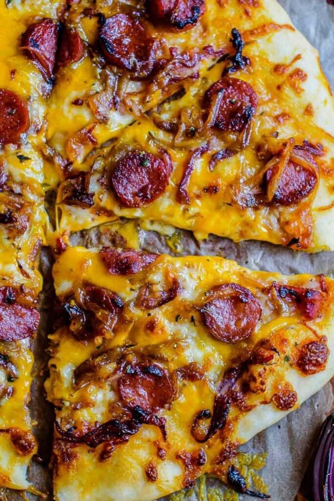 Sliced leftover hot dog pizza with caramelized onions and melted mozzarella on a wooden cutting board