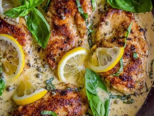 Golden pan-seared lemon chicken in basil cream sauce served in a cast iron skillet garnished with fresh basil and lemon wedges