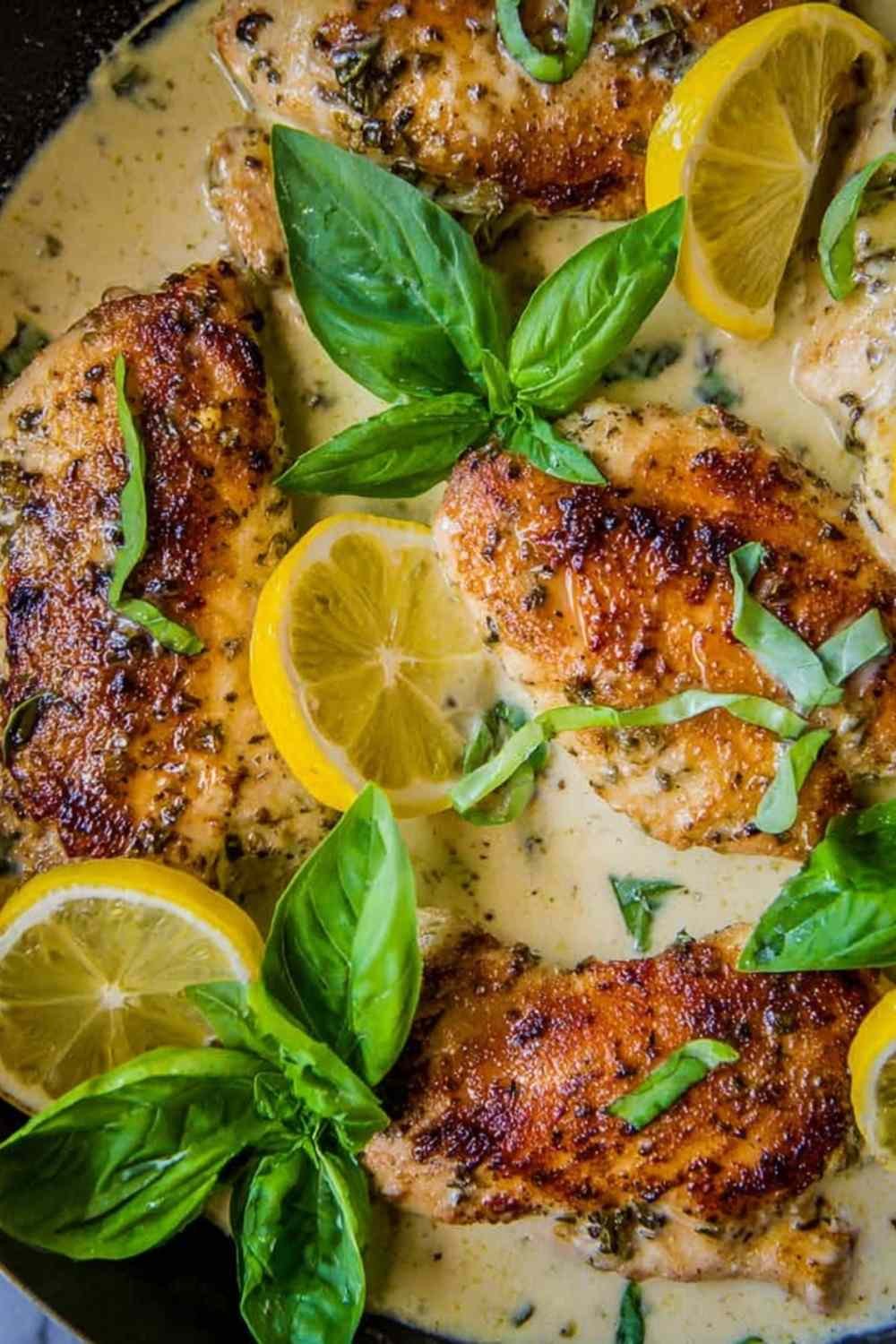 Golden pan-seared lemon chicken in basil cream sauce served in a cast iron skillet garnished with fresh basil and lemon wedges