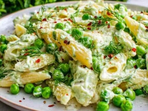 A white plate of lemon pasta with ricotta and fresh peas topped with toasted pine nuts and Parmesan cheese
