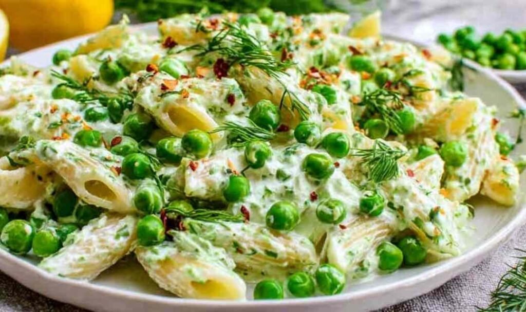 A white plate of lemon pasta with ricotta and fresh peas topped with toasted pine nuts and Parmesan cheese