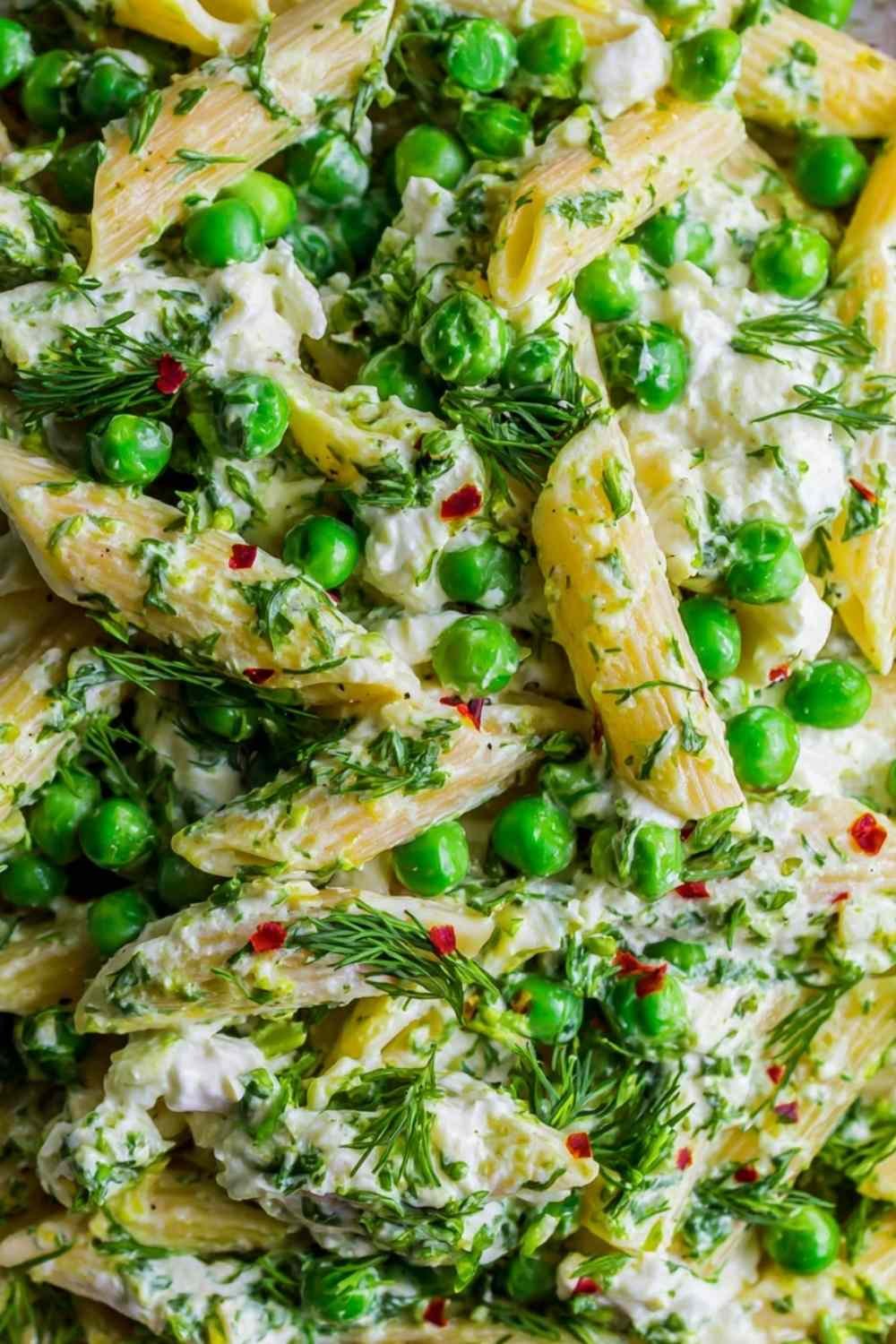 A white plate of lemon pasta with ricotta and fresh peas topped with toasted pine nuts and Parmesan cheese