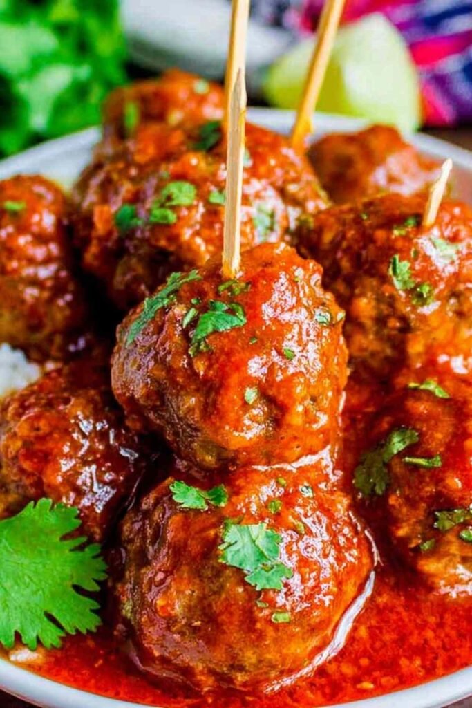 Easy baked Mexican meatballs covered in thick red enchilada sauce and garnished with fresh cilantro, served with cilantro lime rice and pinto beans