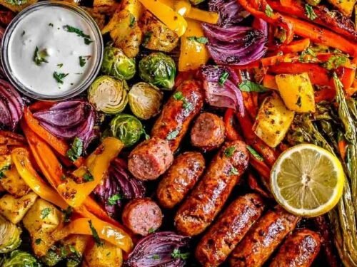 One pan sausage and veggies with lemon aioli on a foil-lined baking sheet fresh out of the oven with caramelized Brussels sprouts, sweet potato, and bratwurst