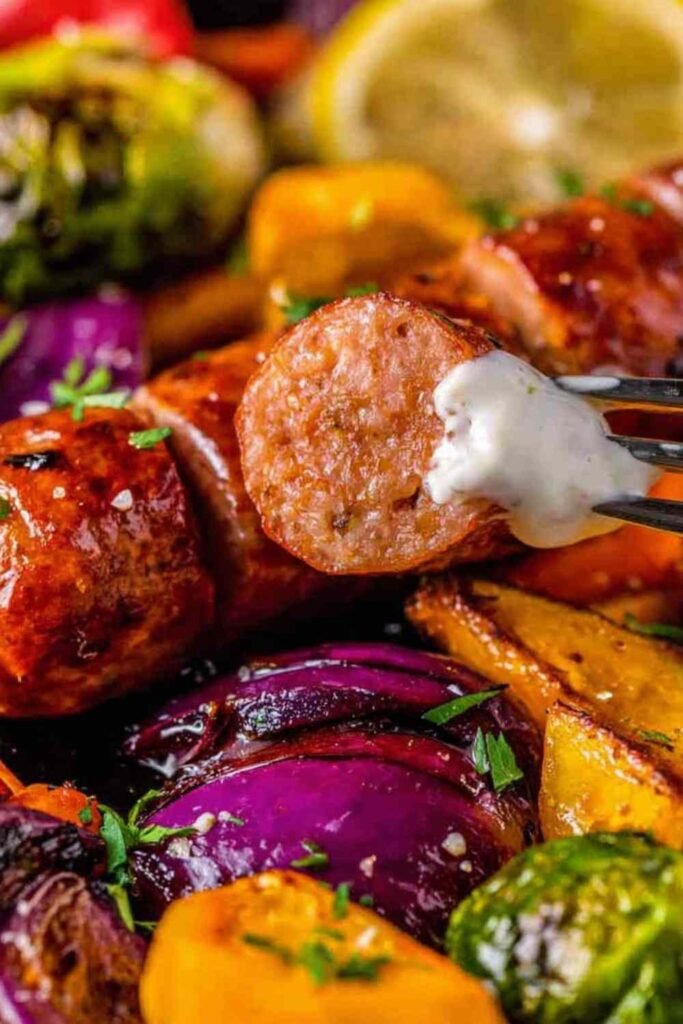 One pan sausage and veggies with lemon aioli on a foil-lined baking sheet fresh out of the oven with caramelized Brussels sprouts, sweet potato, and bratwurst