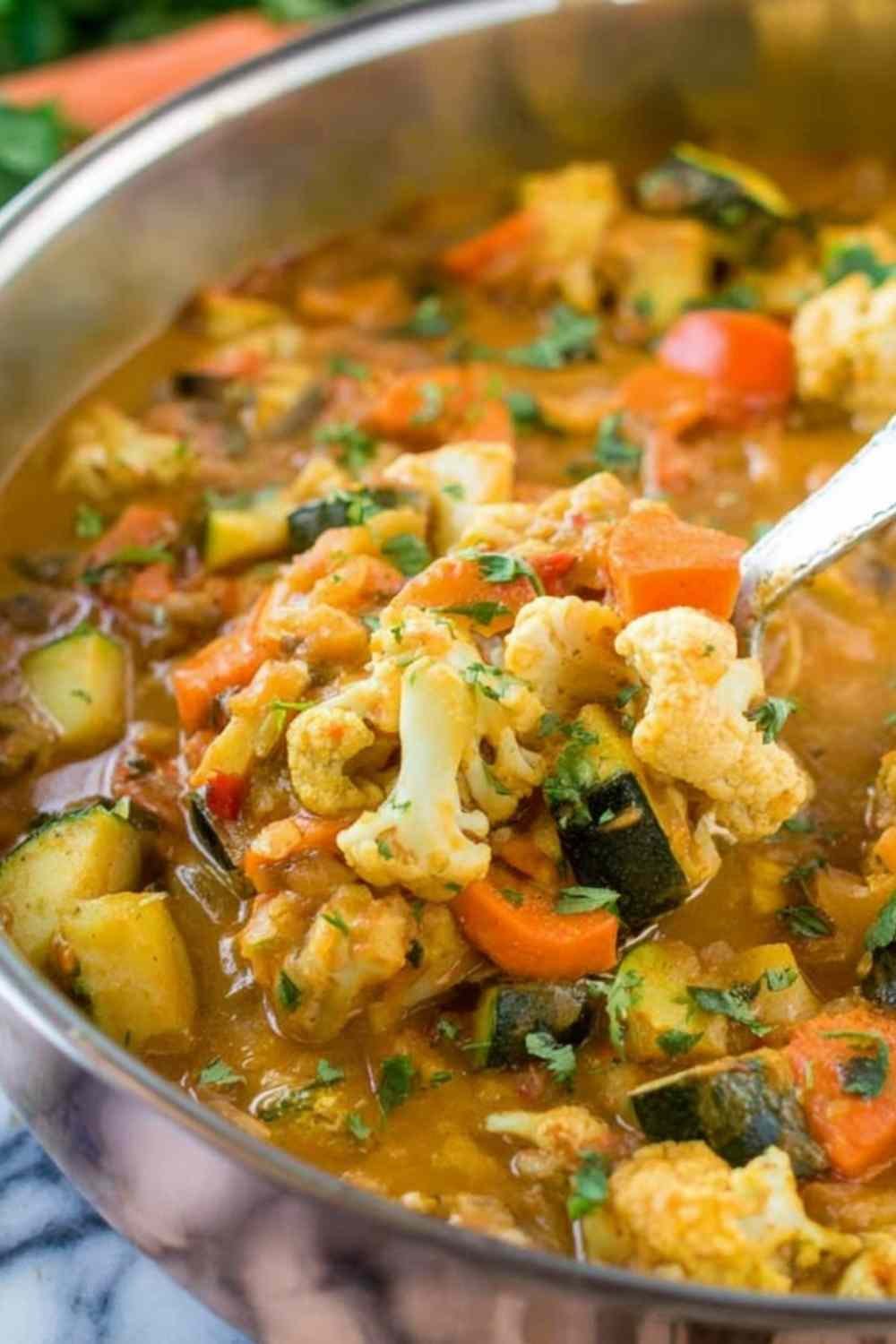 Large pot of one pot vegetable curry simmering with cauliflower, carrots, and zucchini in coconut milk and Indian simmer sauce