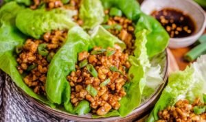 Copycat PF Chang's chicken lettuce wraps filled with diced chicken and shiitake mushrooms served on a white plate with Asian dipping sauce