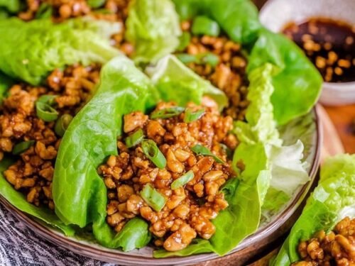 Copycat PF Chang's chicken lettuce wraps filled with diced chicken and shiitake mushrooms served on a white plate with Asian dipping sauce