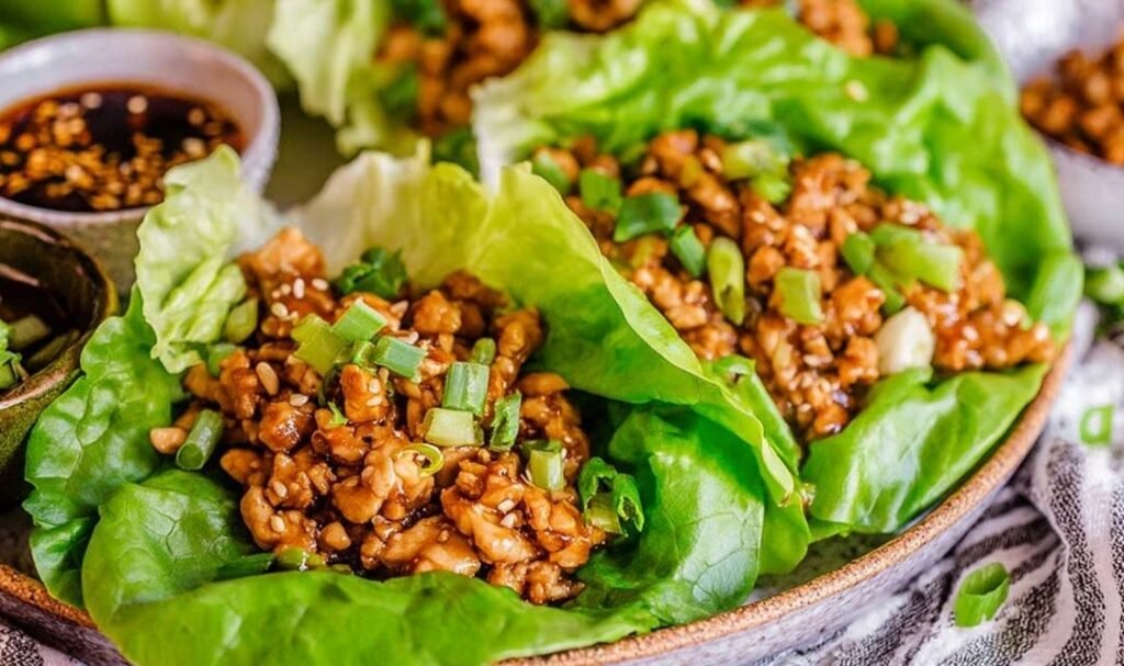 Copycat PF Chang's chicken lettuce wraps filled with diced chicken and shiitake mushrooms served on a white plate with Asian dipping sauce