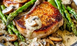 Pan seared pork chops with creamy mushroom sauce, asparagus, and fresh thyme in a cast iron skillet