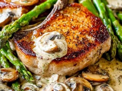 Pan seared pork chops with creamy mushroom sauce, asparagus, and fresh thyme in a cast iron skillet