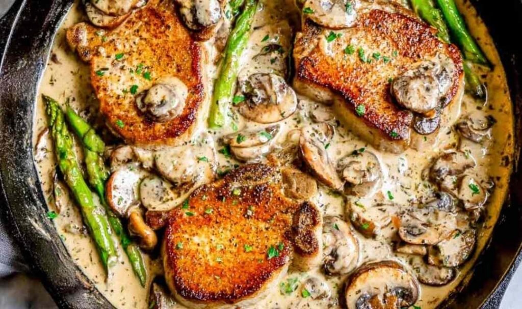 Pan seared pork chops with creamy mushroom sauce, asparagus, and fresh thyme in a cast iron skillet