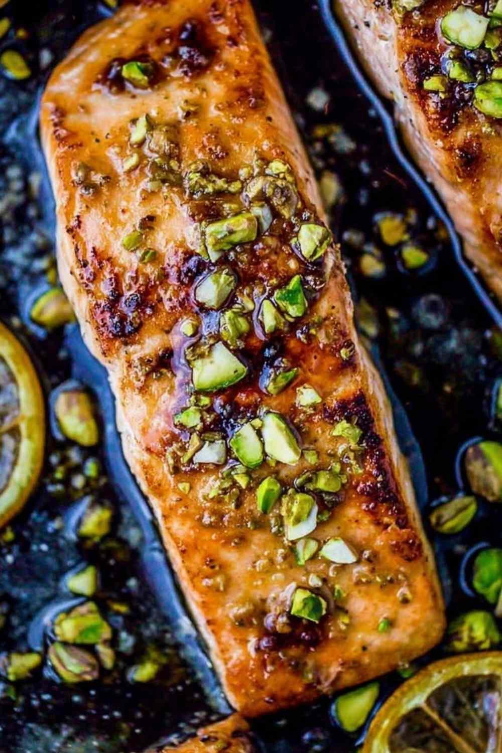 Two golden pan-seared salmon fillets with maple glaze in a cast iron skillet topped with chopped pistachios