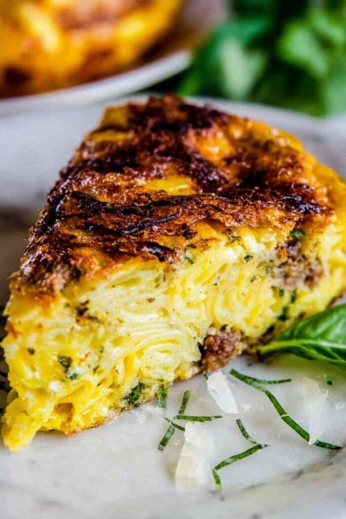 Golden pasta frittata with sausage and parmesan in a nonstick skillet, crispy edges visible