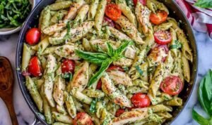Creamy pesto penne with chicken and cherry tomatoes served in a white bowl garnished with shredded Parmesan