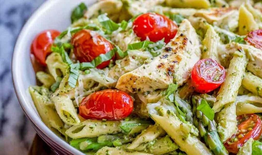 Creamy pesto penne with chicken and cherry tomatoes served in a white bowl garnished with shredded Parmesan