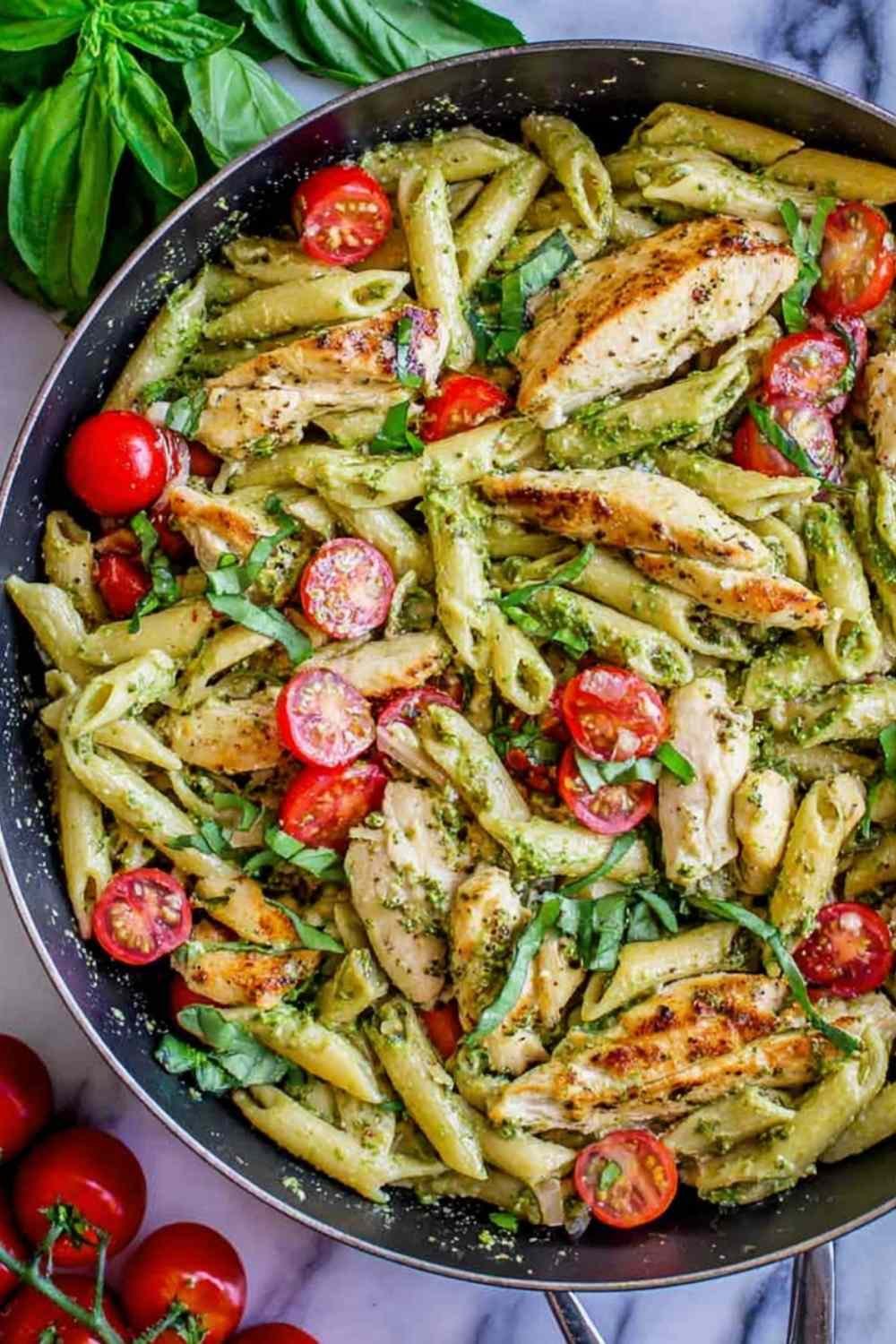 Creamy pesto penne with chicken and cherry tomatoes served in a white bowl garnished with shredded Parmesan