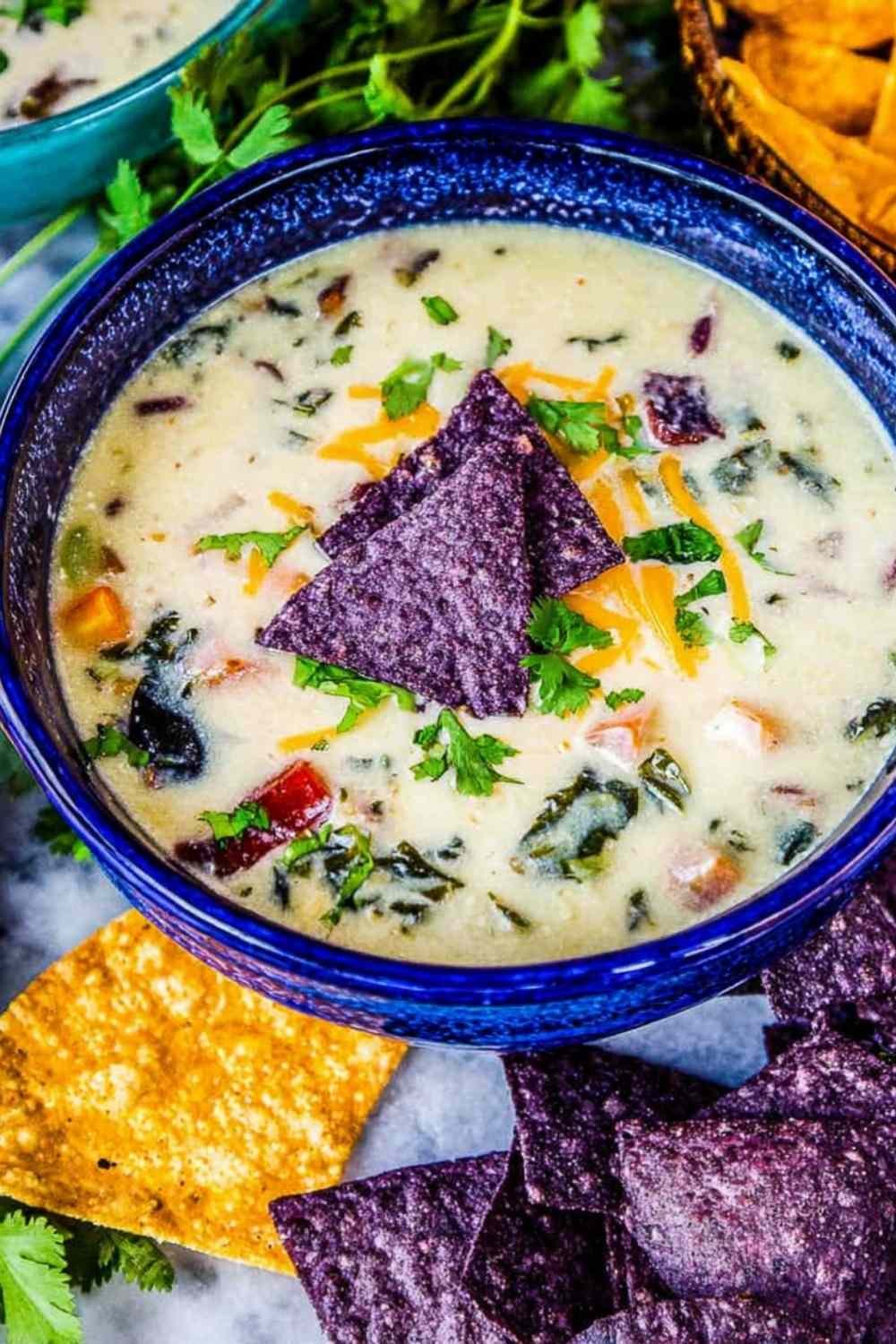 A bowl of creamy queso dip potato soup topped with blue tortilla chips, sliced jalapeno, red onion, and fresh cilantro