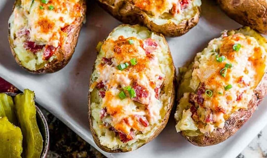 Reuben stuffed twice baked potatoes topped with melted Swiss cheese and garnished with chopped dill pickles on a greased sheet pan