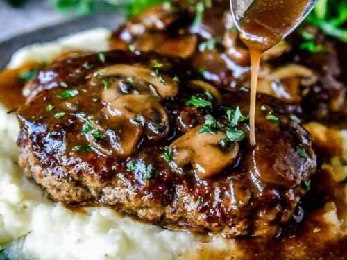 Homemade Salisbury steak recipe with mushroom gravy simmering in a cast iron skillet garnished with fresh parsley