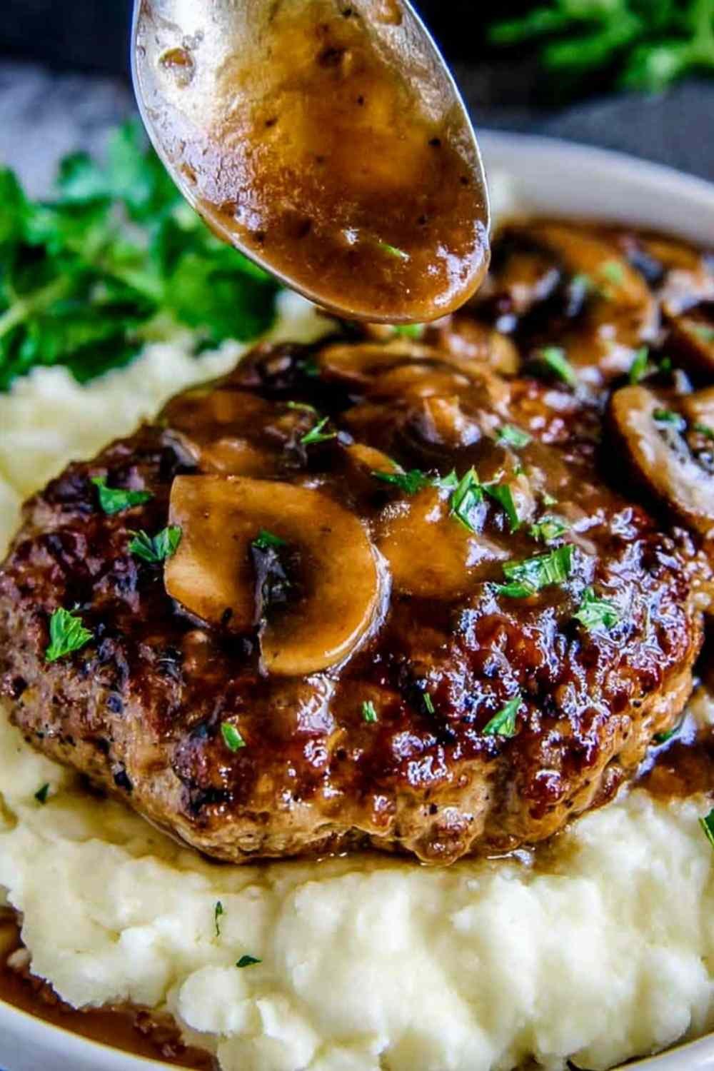 Homemade Salisbury steak recipe with mushroom gravy simmering in a cast iron skillet garnished with fresh parsley