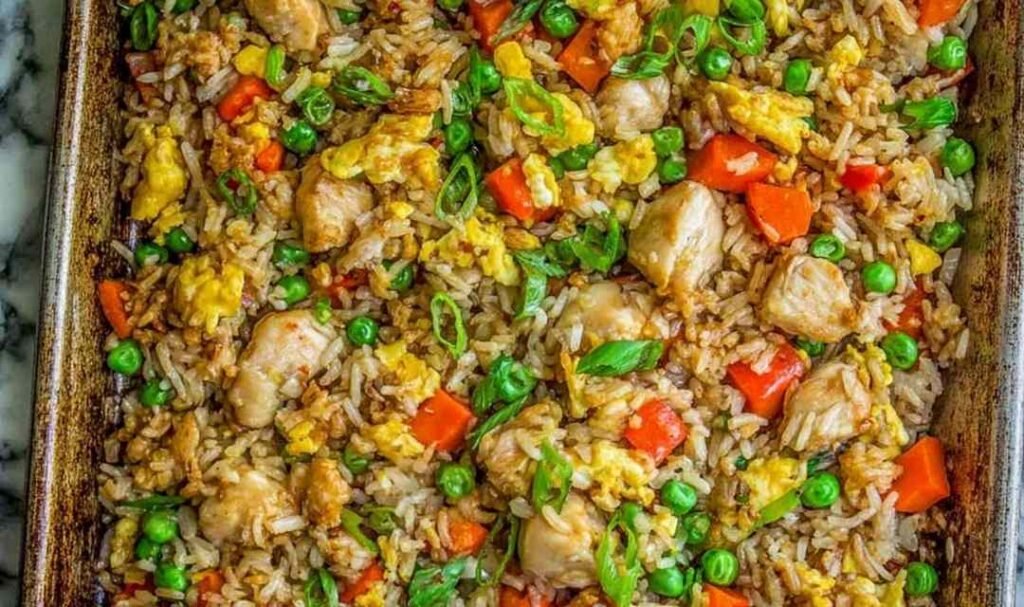 Sheet pan chicken fried rice with peas, carrots, red bell pepper, and green onions fresh out of the oven