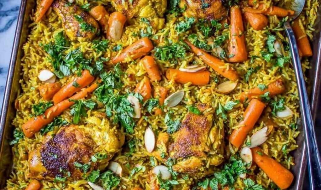 Sheet pan curry chicken with roasted carrots, basmati rice, cashews, and cilantro on a rimmed baking sheet