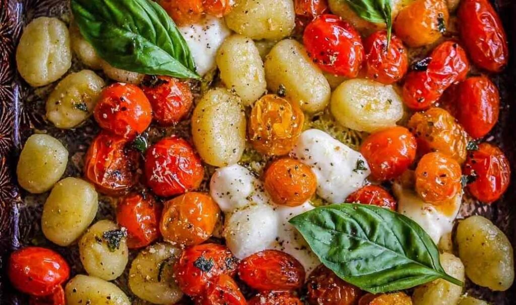 Sheet pan gnocchi with cherry tomatoes and mozzarella garnished with fresh basil and Parmesan on a parchment-lined baking sheet