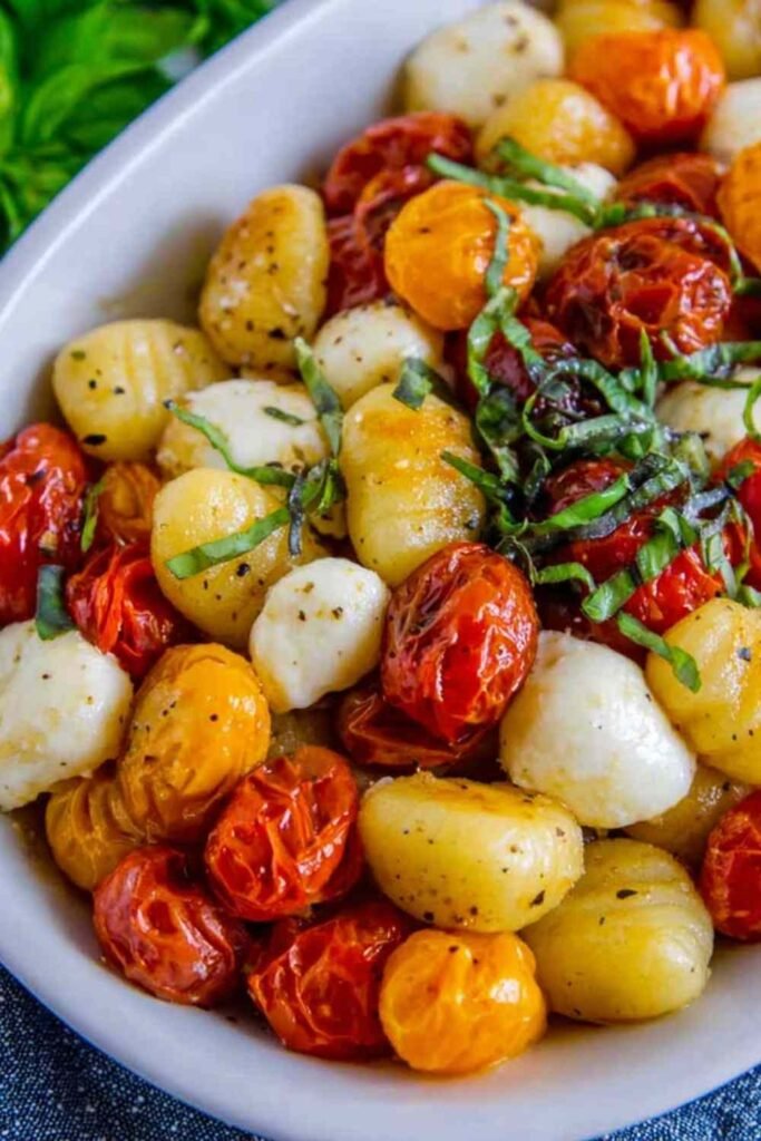 Sheet pan gnocchi with cherry tomatoes and mozzarella garnished with fresh basil and Parmesan on a parchment-lined baking sheet