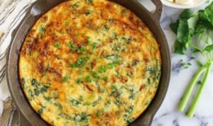 Golden spinach bacon frittata in a cast iron skillet topped with green onions and melted gouda cheese