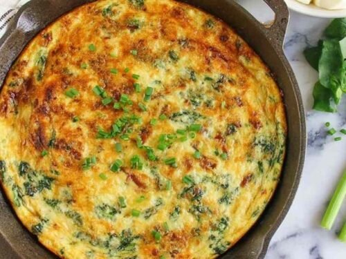 Golden spinach bacon frittata in a cast iron skillet topped with green onions and melted gouda cheese