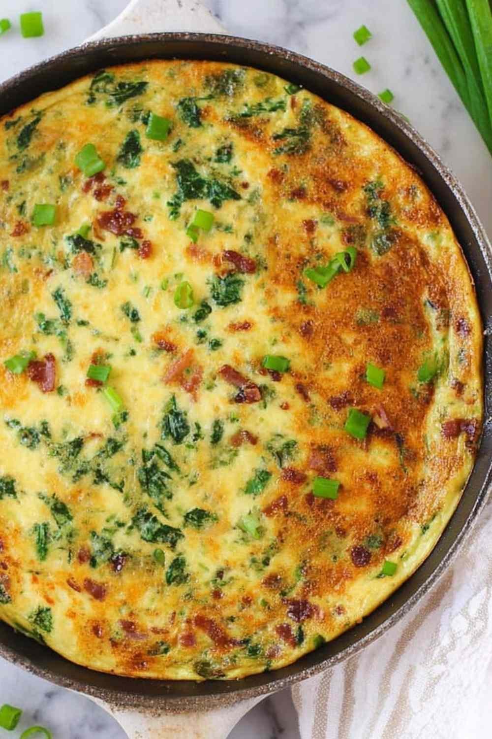 Golden spinach bacon frittata in a cast iron skillet topped with green onions and melted gouda cheese