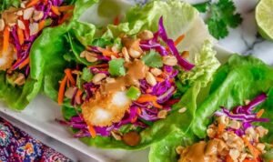 Hands assembling Thai Peanut Lettuce Wraps with crispy fish and fresh cabbage slaw