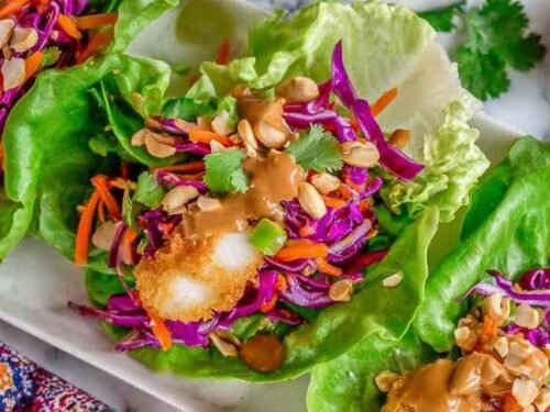 Hands assembling Thai Peanut Lettuce Wraps with crispy fish and fresh cabbage slaw