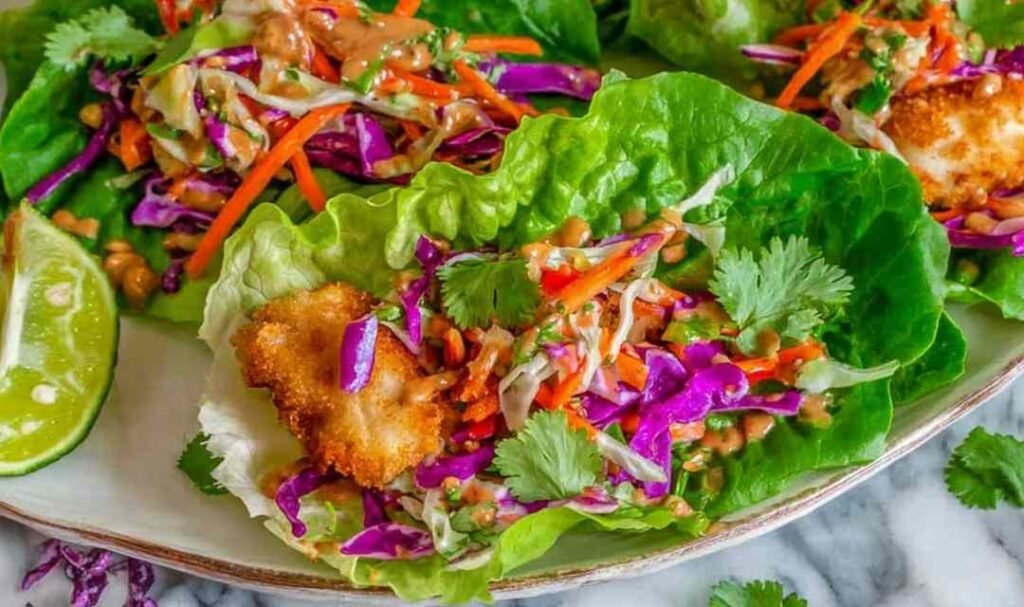 Hands assembling Thai Peanut Lettuce Wraps with crispy fish and fresh cabbage slaw