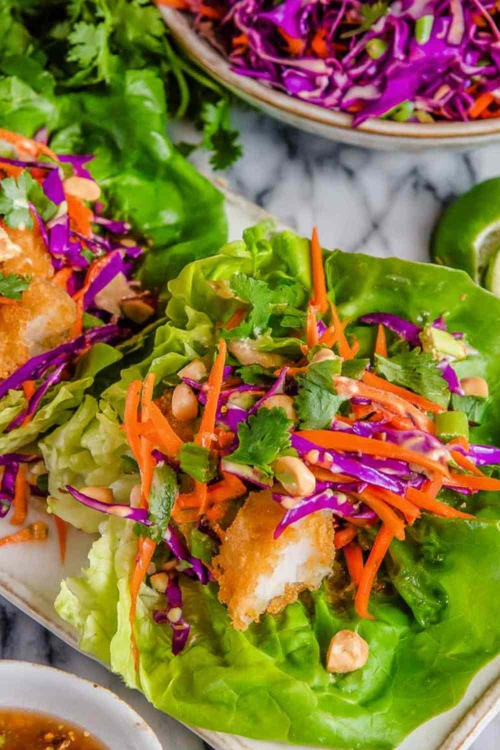 Hands assembling Thai Peanut Lettuce Wraps with crispy fish and fresh cabbage slaw