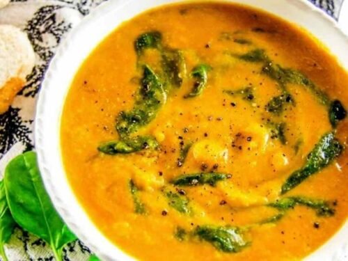 A white bowl of creamy vegan cauliflower soup topped with fresh spinach and freshly ground black pepper