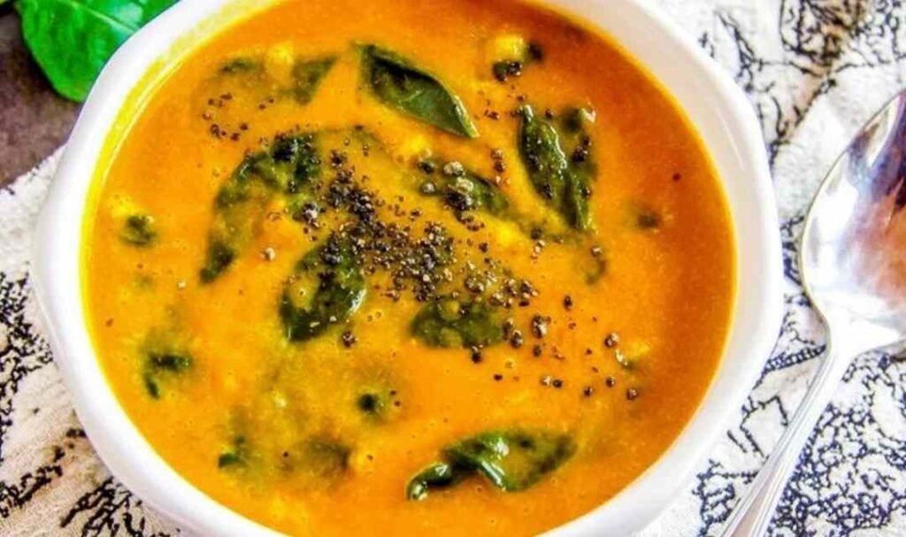 A white bowl of creamy vegan cauliflower soup topped with fresh spinach and freshly ground black pepper