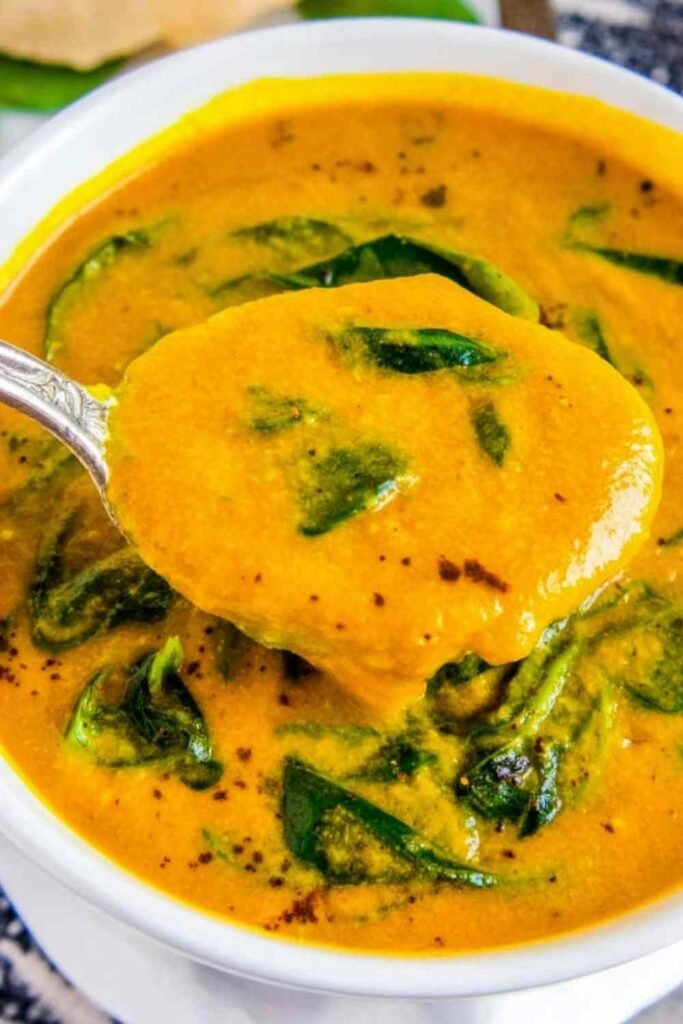 A white bowl of creamy vegan cauliflower soup topped with fresh spinach and freshly ground black pepper